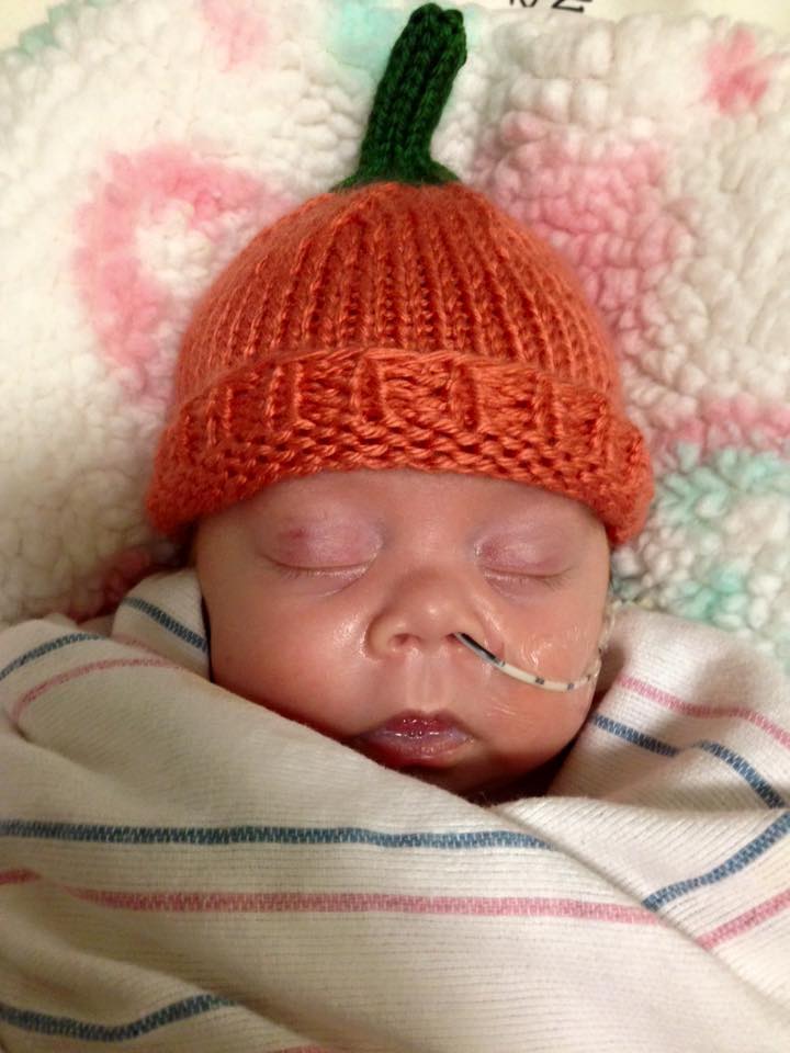 A baby wearing an orange hat is sleeping.
