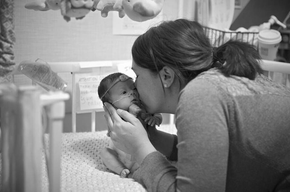 A woman kissing her baby in the bed.