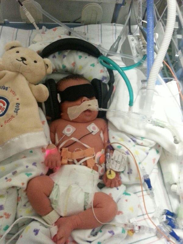 A baby with headphones and teddy bear in hospital.