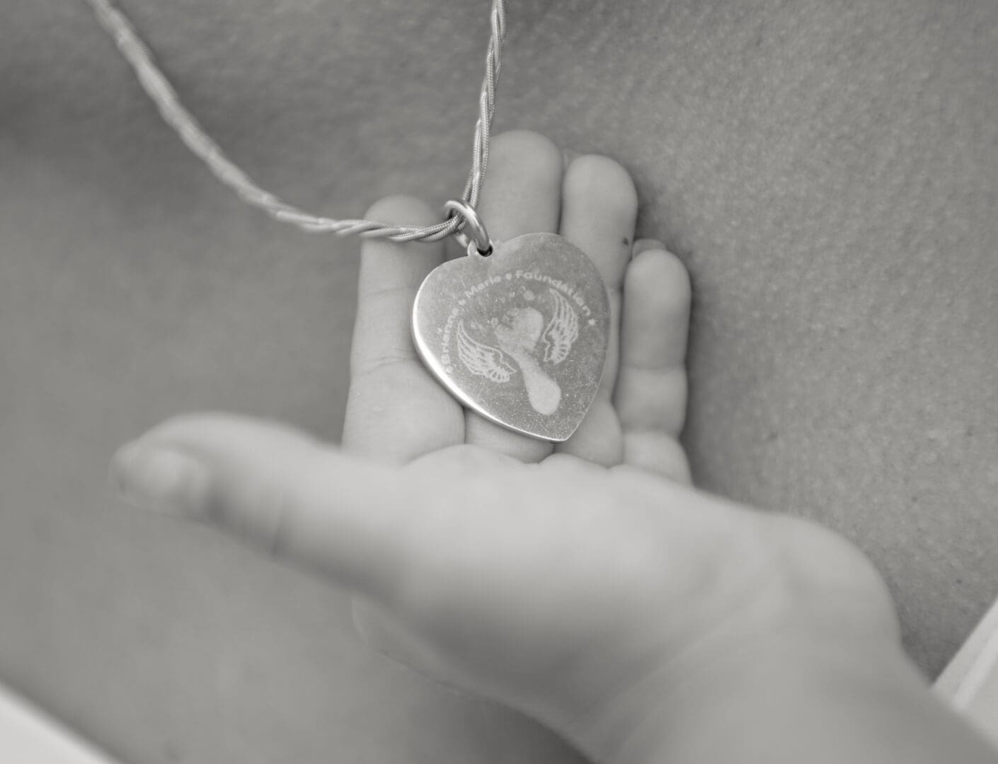 A child 's hand holding a heart shaped necklace.