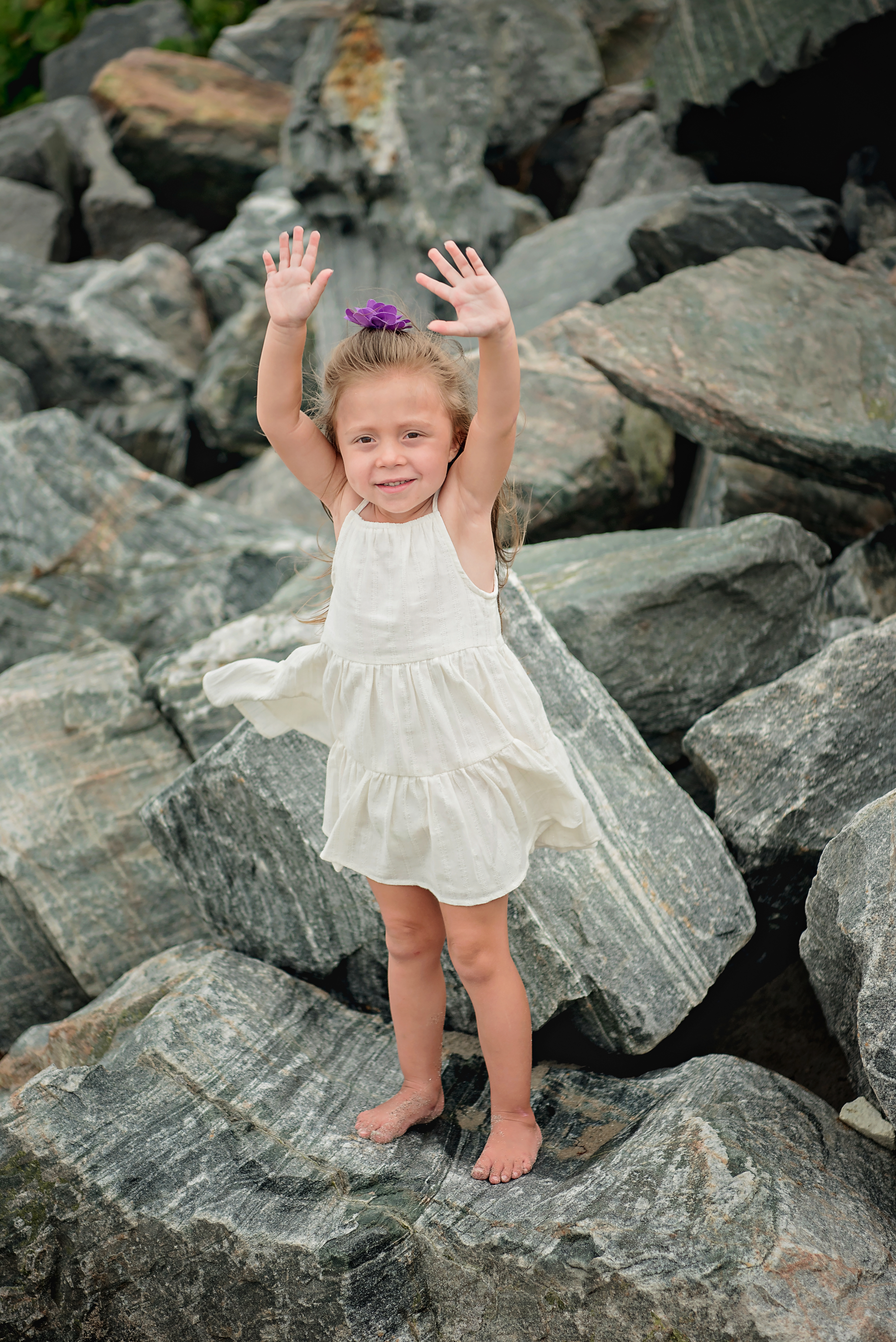 A little girl standing on some rocks with her hands up